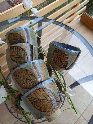 Kubki inspiracji - nagroda Trójmiejskiego Parku Krajobrazowego za motywy przyrodnicze w piosence (fot. Anna Moś) Pięć kubków leżących na szklanym stoliku, włożone jeden w drugi, na kubkach namalowane liście.