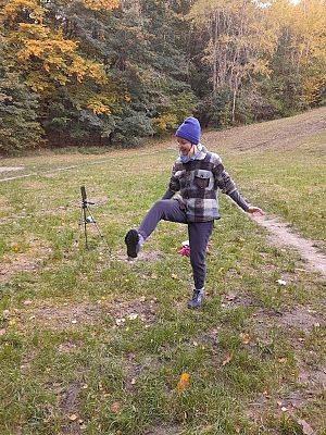 Najpierw rozgrzewka (fot. A. Kowalewska) Na zdjęciu tańcząca na trawie kobieta z podniesioną prawą nogą, w tle przebarwione na żółto drzewa.