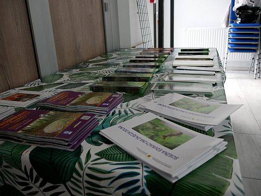 Na stole z kolorowym obrusem leżą materiały edukacyjne i promocyjne Trójmiejskiego Parku Krajobrazowego (TPK): niewielkie broszury o tematyce ptaków, płazów, gadów, pomników przyrody, użytków ekologicznych znajdujących się na terenie TPK.